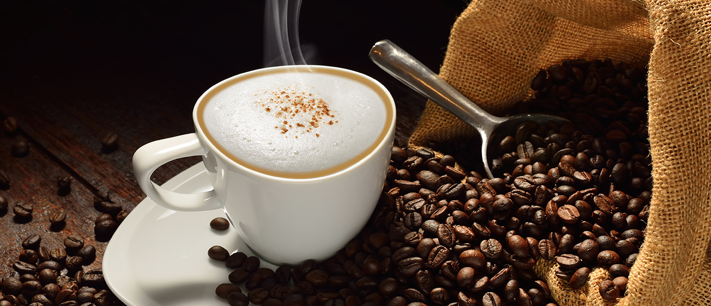 A warm cup of coffee sits atop a pile of beans.