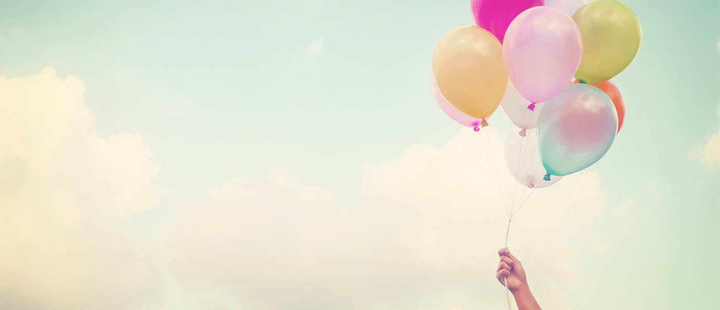 hand holding balloons with the sky in the background