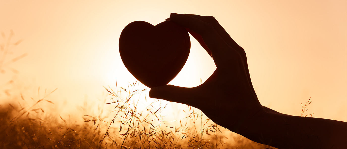 A hand holding up a heart shape against the sun