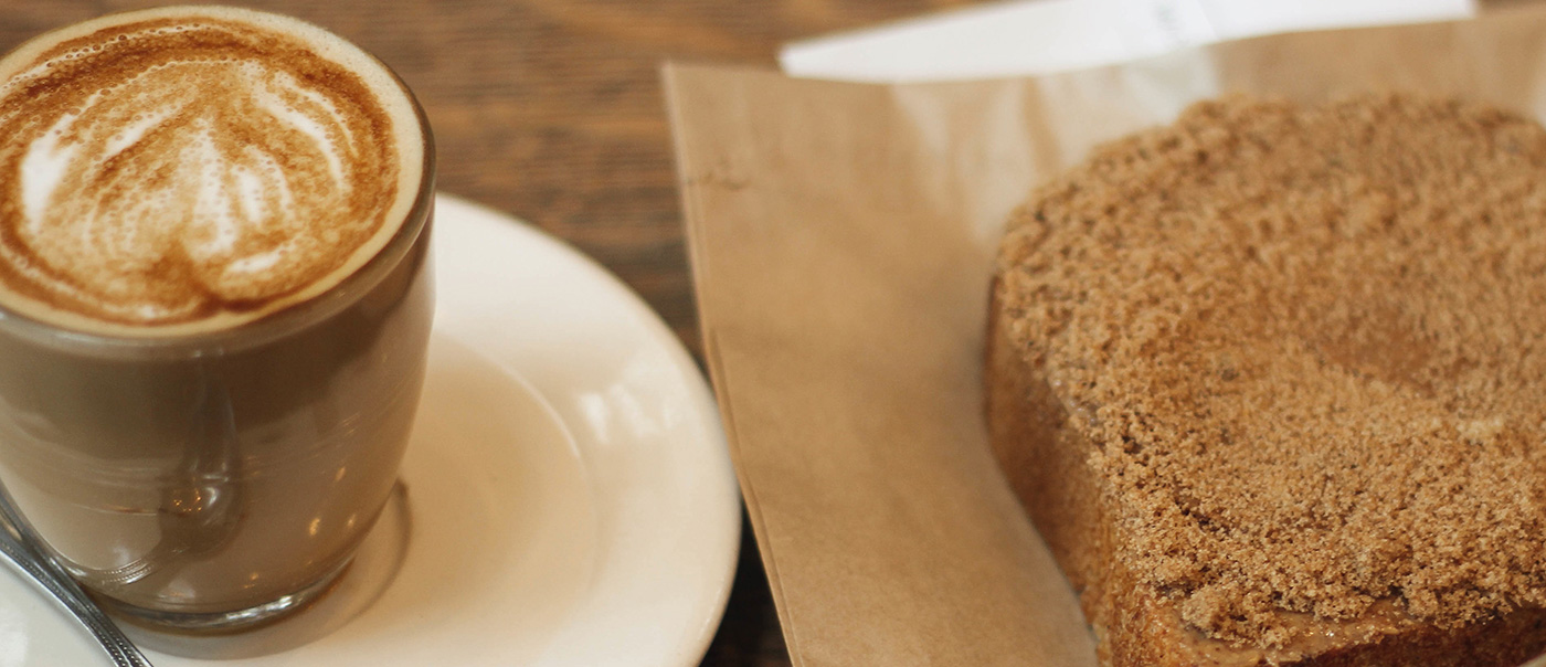 A warm drink next to a piece of bread.