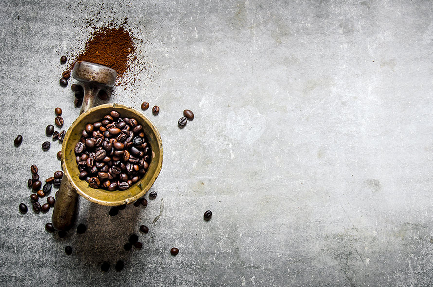 Cup of coffee beans next to press