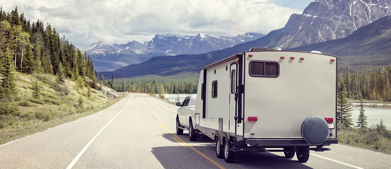 Truck pulling a trailer on a road surrounded by mountains