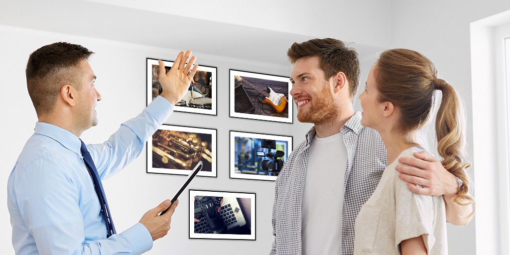 A REALTOR(r) shows a home to a young couple. Photographs hang on the walls