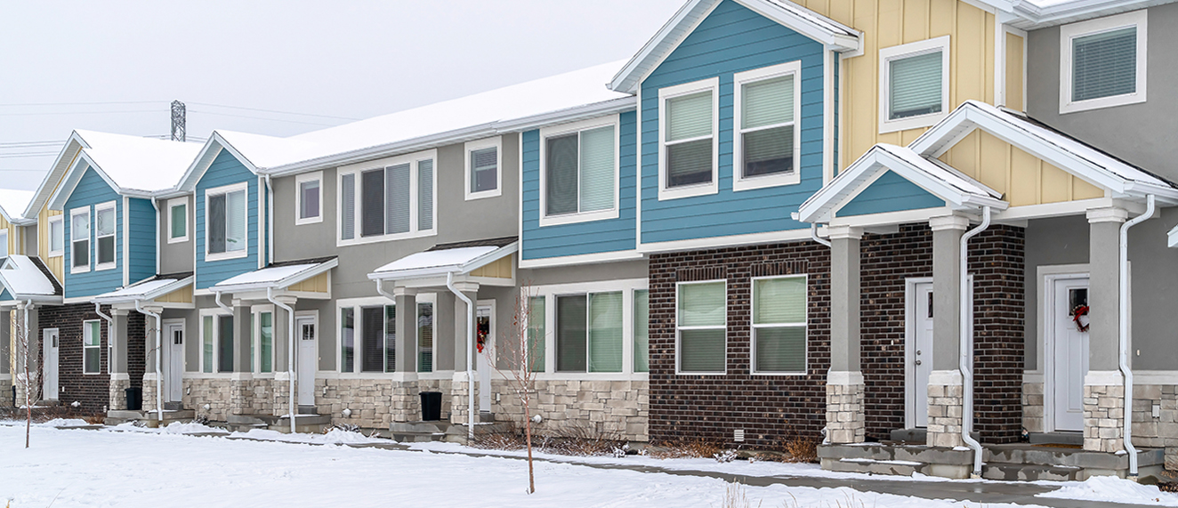 Two storey apartments on a beautiful residential landscape with snow in winter. The houses have colorful walls and white doors at the frnt entrances with roofs.