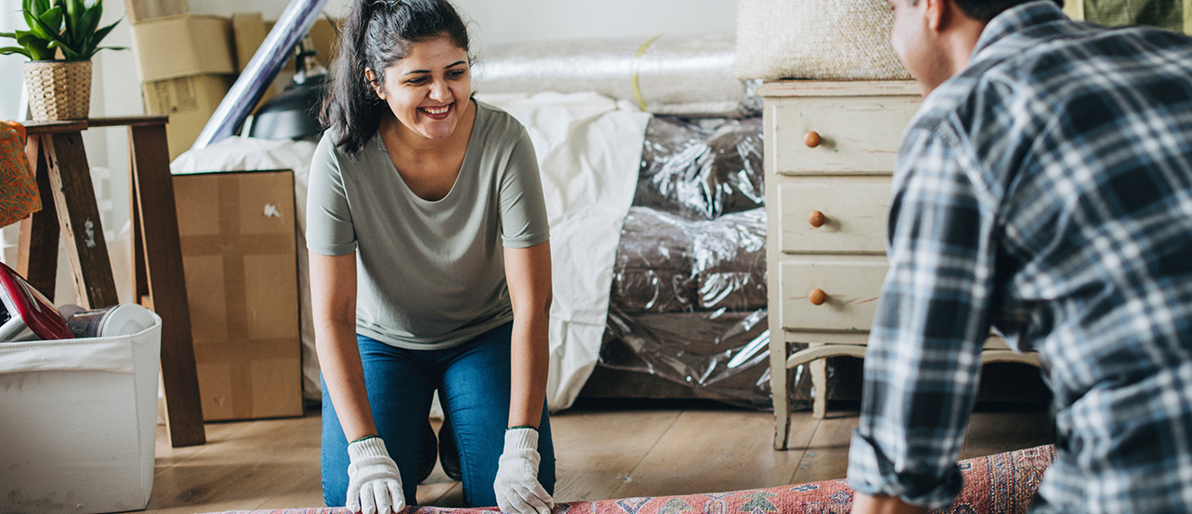 Couple unroll carpet together in new home.