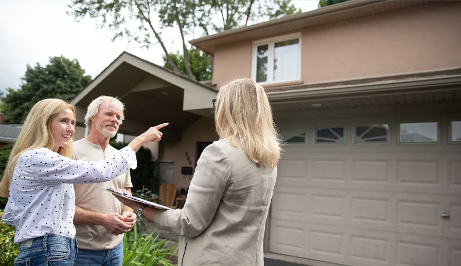 Couple with real estate agent standing outside of home. 