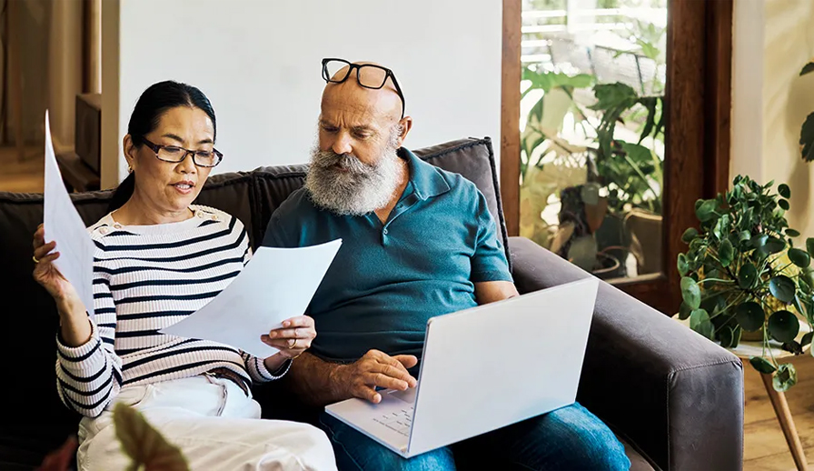 Couple looking over papers and laptop on couch.