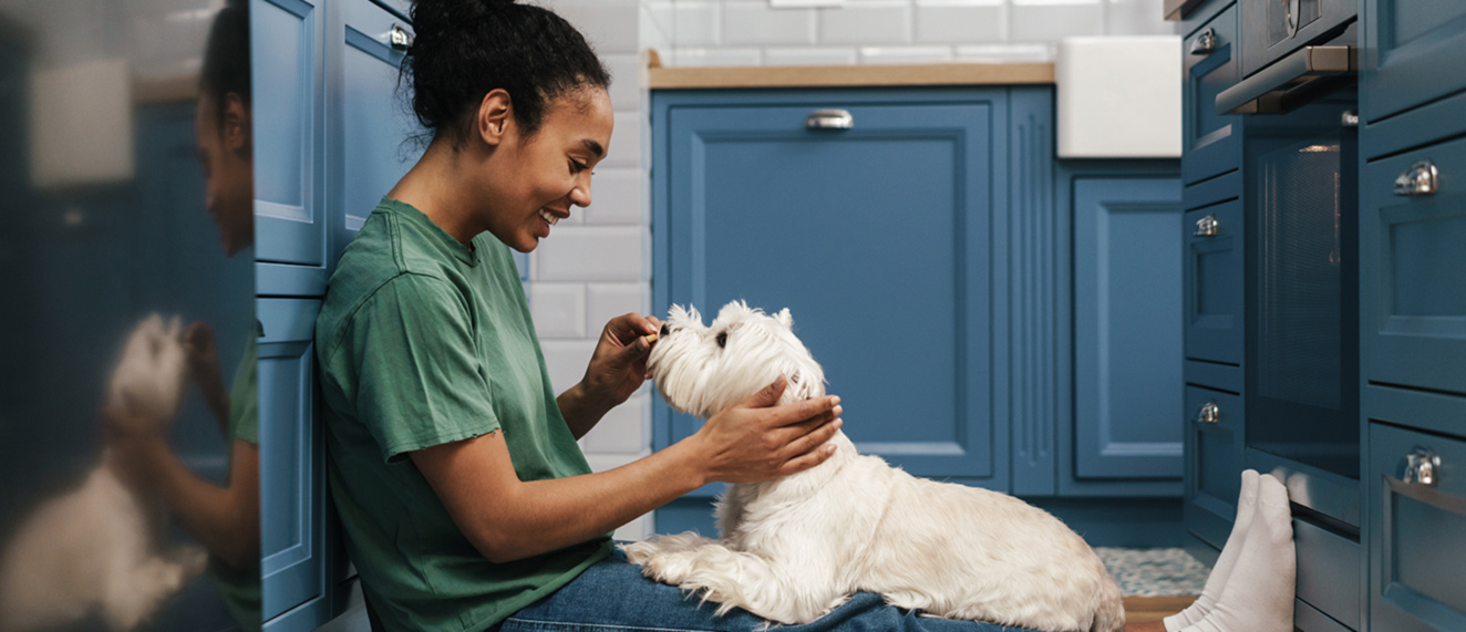 Woman giving dog a treat in kitchen.