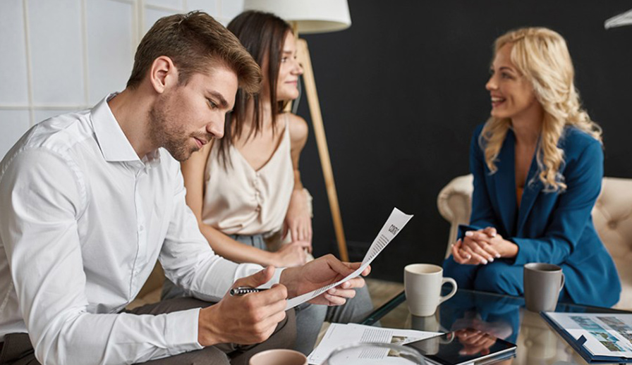 Three people talking over documents on couch. 