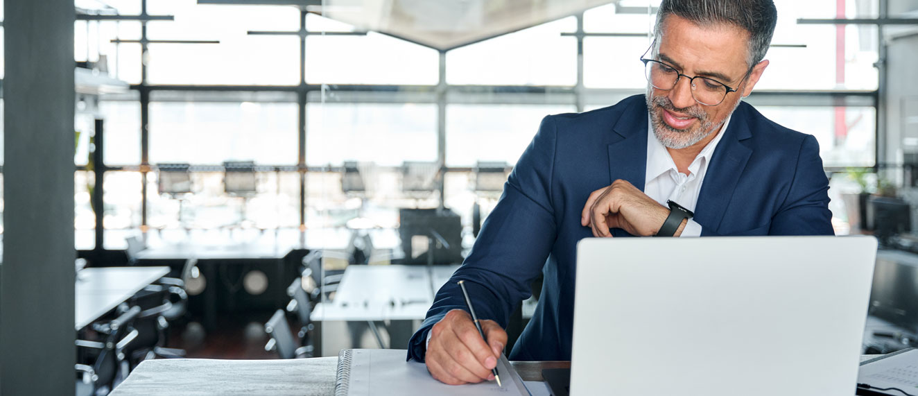 Man writing notes while sitting in front of a laptop.